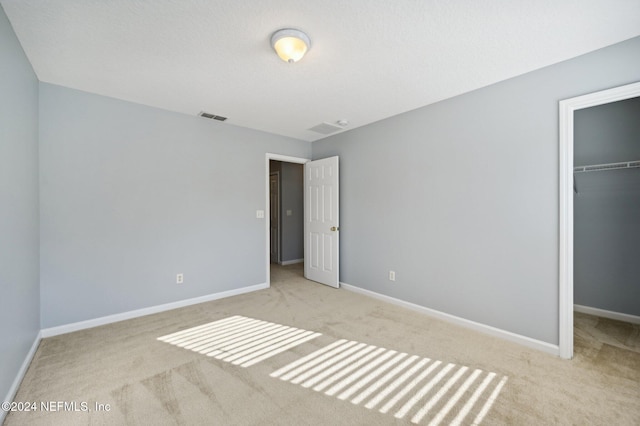 unfurnished bedroom featuring a spacious closet, light carpet, and a closet