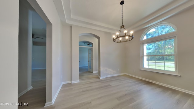 empty room with light hardwood / wood-style floors, a raised ceiling, and ceiling fan