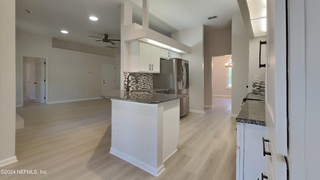 kitchen with sink, white cabinetry, dark stone countertops, stainless steel refrigerator with ice dispenser, and kitchen peninsula