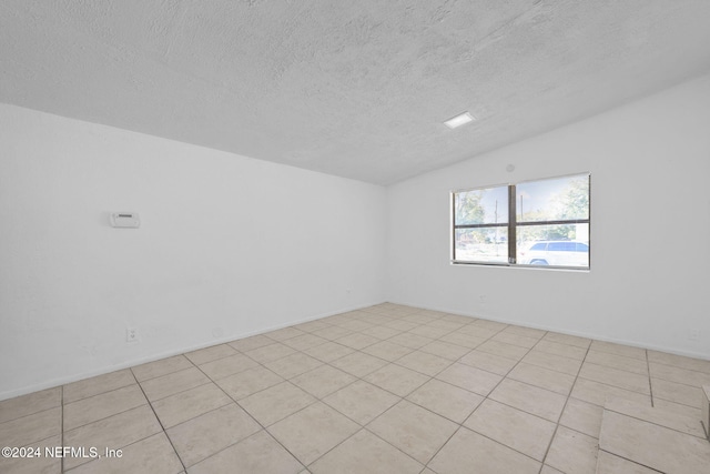 empty room featuring lofted ceiling, a textured ceiling, and light tile patterned floors