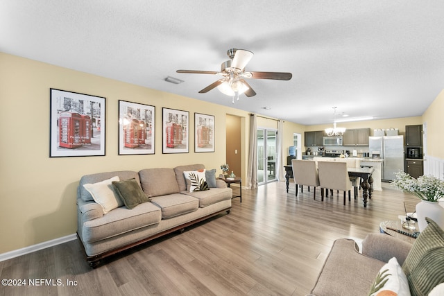 living room with ceiling fan with notable chandelier, light hardwood / wood-style floors, and a textured ceiling