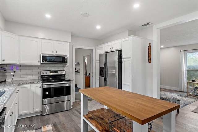 kitchen featuring light stone countertops, decorative backsplash, stainless steel appliances, dark wood-type flooring, and white cabinetry