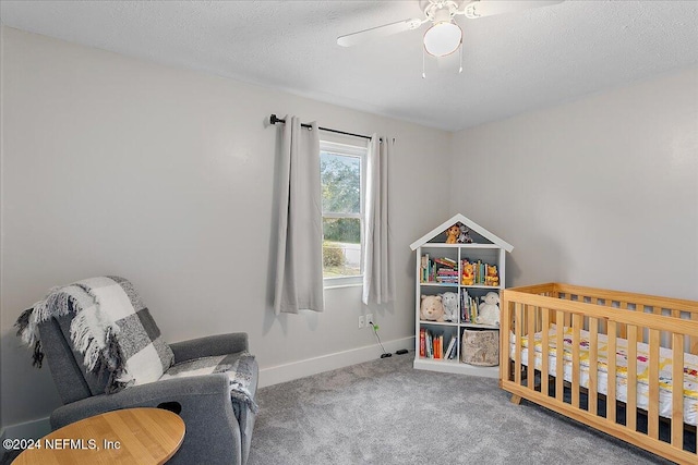 carpeted bedroom with ceiling fan, a crib, and a textured ceiling