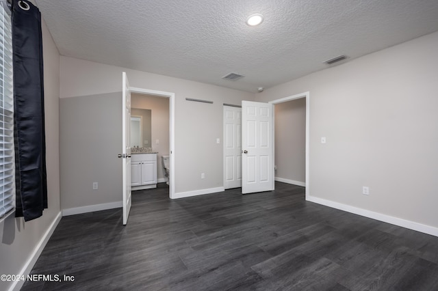 unfurnished bedroom with a textured ceiling, connected bathroom, and dark hardwood / wood-style floors