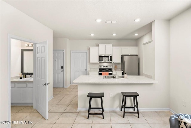 kitchen featuring appliances with stainless steel finishes, sink, light tile patterned floors, white cabinets, and a breakfast bar area