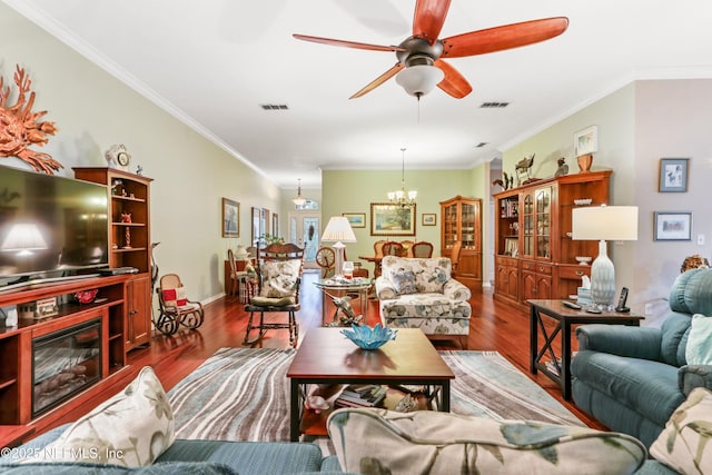 living room featuring ceiling fan with notable chandelier, ornamental molding, and dark wood-type flooring