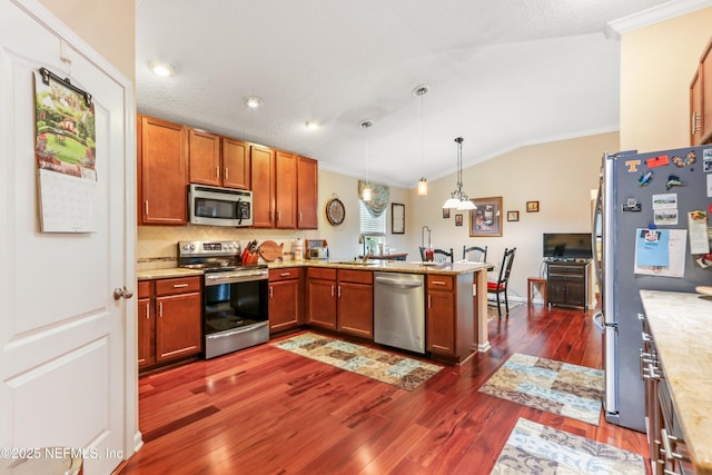 kitchen featuring kitchen peninsula, hanging light fixtures, lofted ceiling, appliances with stainless steel finishes, and ornamental molding