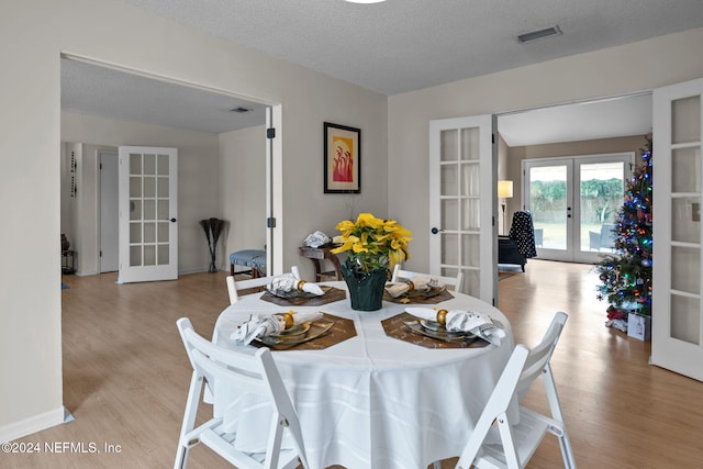 dining area with french doors, light hardwood / wood-style floors, and a textured ceiling