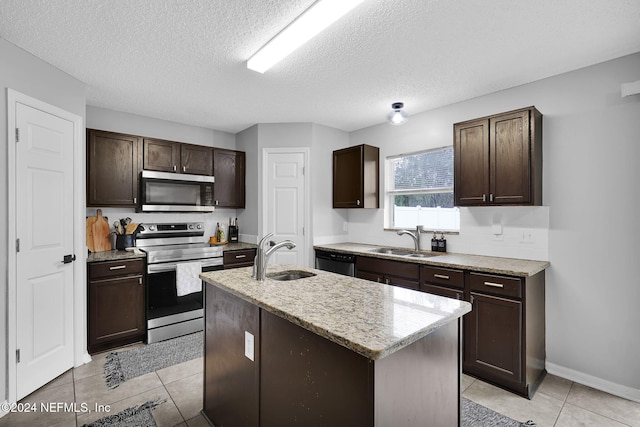 kitchen featuring dark brown cabinets, sink, appliances with stainless steel finishes, and an island with sink