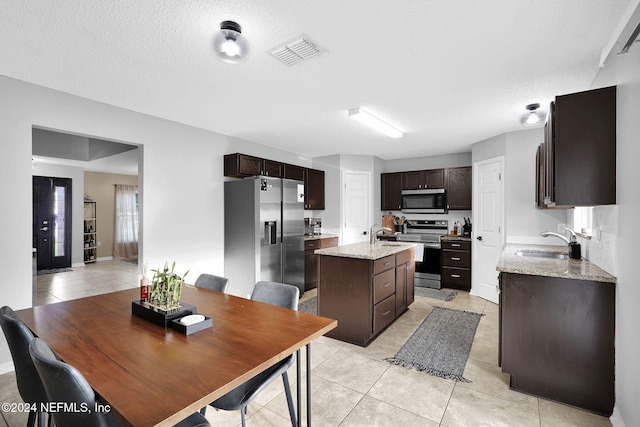 kitchen with a center island with sink, sink, a textured ceiling, appliances with stainless steel finishes, and light stone counters