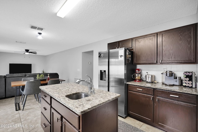 kitchen with stainless steel fridge, a textured ceiling, ceiling fan, a kitchen island with sink, and sink