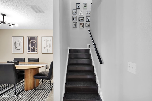 stairs with a notable chandelier and a textured ceiling