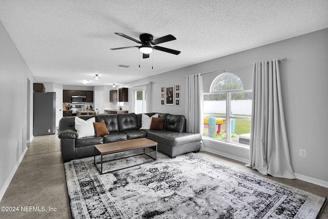 living room featuring ceiling fan, light tile patterned flooring, and a textured ceiling