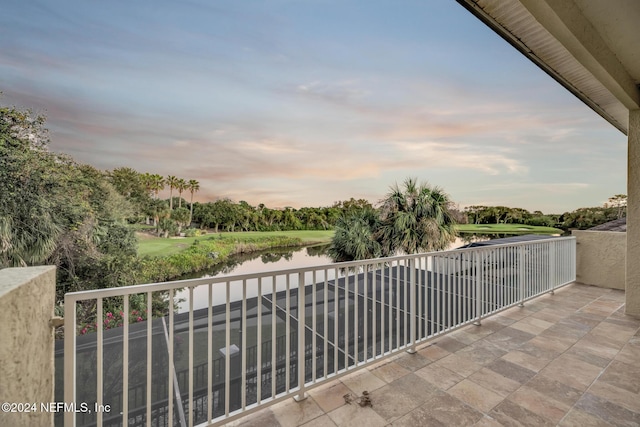 balcony at dusk featuring a water view