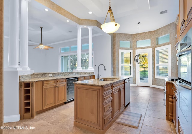 kitchen with hanging light fixtures, sink, ornate columns, an island with sink, and beverage cooler