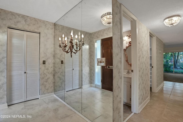 hall featuring sink, light tile patterned floors, a textured ceiling, and an inviting chandelier