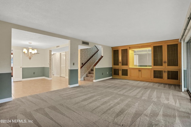 unfurnished living room with a chandelier, a textured ceiling, and light colored carpet