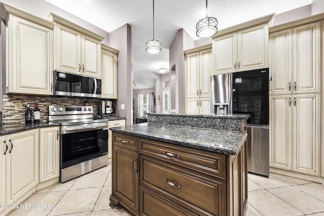 kitchen with dark stone countertops, hanging light fixtures, light tile patterned floors, stainless steel appliances, and cream cabinetry