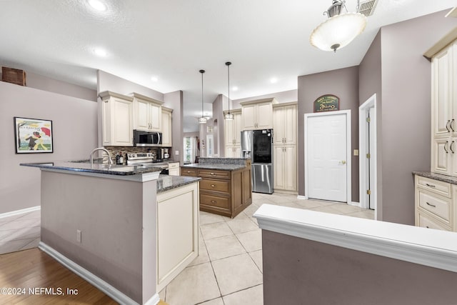 kitchen featuring a kitchen island, appliances with stainless steel finishes, pendant lighting, dark stone counters, and cream cabinets