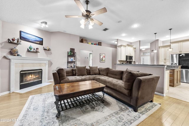 living room featuring a tiled fireplace, light hardwood / wood-style floors, and ceiling fan