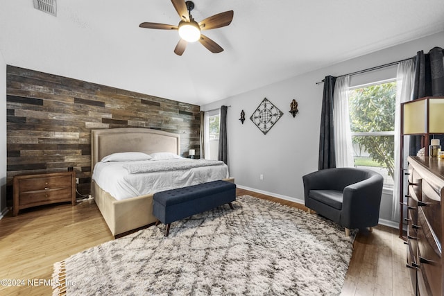 bedroom with ceiling fan, wood-type flooring, and wood walls