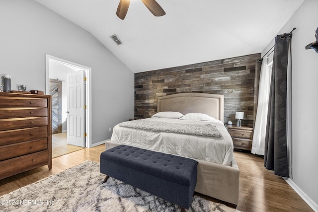 bedroom with wood-type flooring, lofted ceiling, ceiling fan, and wooden walls