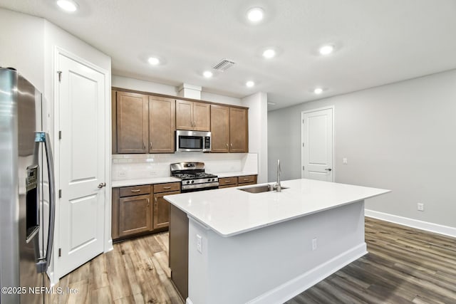 75484 Banyan Way, Yulee, FL 32097 - kitchen featuring stainless steel appliances, wood finished floors, a sink, an island with sink, and backsplash