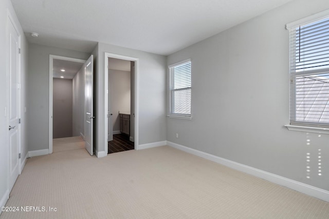 unfurnished bedroom featuring ensuite bath and light colored carpet