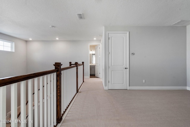 corridor with light carpet and a textured ceiling