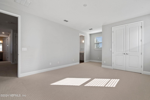 unfurnished bedroom with ensuite bathroom, a closet, and light colored carpet