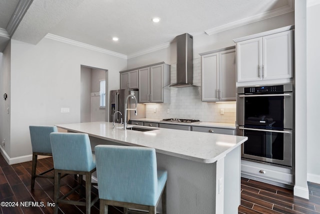 kitchen with a center island with sink, dark hardwood / wood-style floors, wall chimney range hood, and appliances with stainless steel finishes