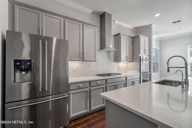 kitchen with light stone counters, gray cabinetry, wall chimney exhaust hood, stainless steel appliances, and sink