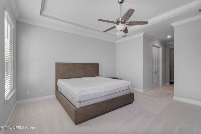 carpeted bedroom featuring ceiling fan, ornamental molding, a tray ceiling, and multiple windows