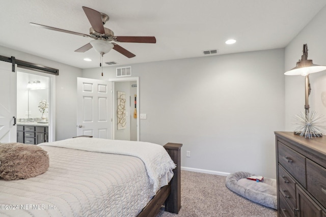 bedroom featuring ceiling fan, a barn door, light carpet, and ensuite bath