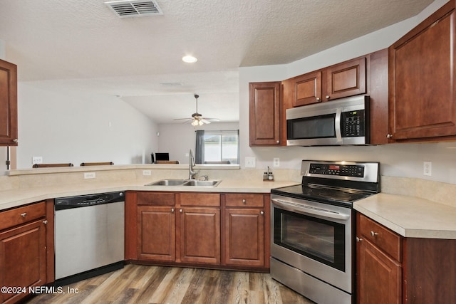 kitchen with lofted ceiling, sink, kitchen peninsula, wood-type flooring, and stainless steel appliances