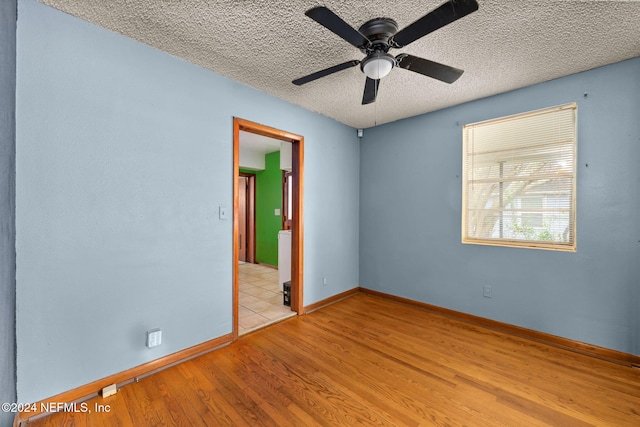 unfurnished room with ceiling fan, a textured ceiling, and light wood-type flooring