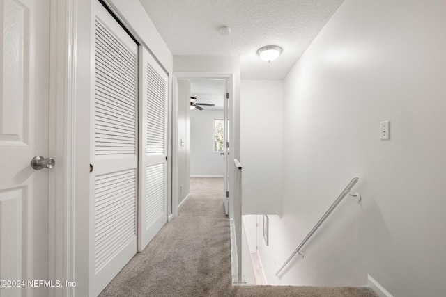 hall with baseboards, an upstairs landing, a textured ceiling, and carpet floors