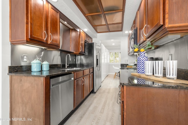 kitchen featuring light wood-style flooring, a sink, dark stone countertops, appliances with stainless steel finishes, and baseboards