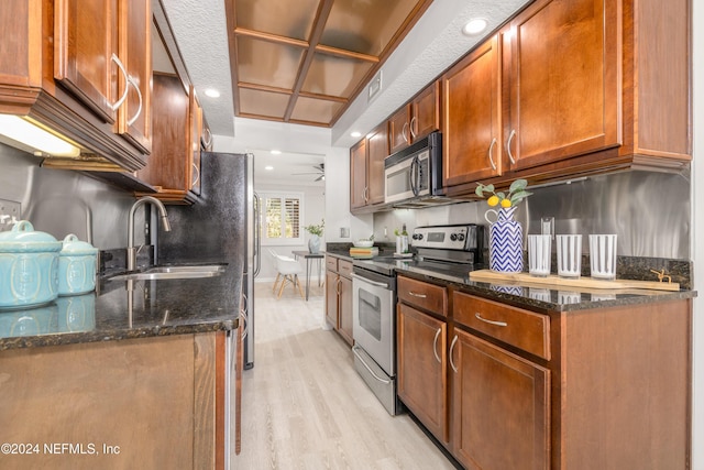 kitchen with light wood-style flooring, stainless steel appliances, dark stone counters, and a sink