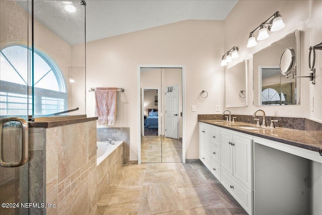 ensuite bathroom with double vanity, a relaxing tiled tub, vaulted ceiling, and a sink