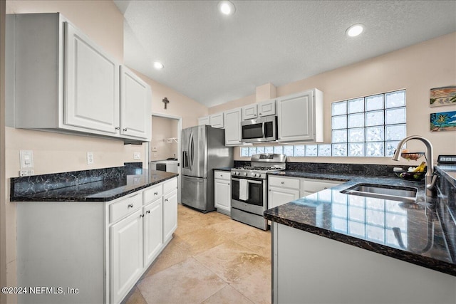 kitchen with dark stone countertops, white cabinetry, stainless steel appliances, and a sink