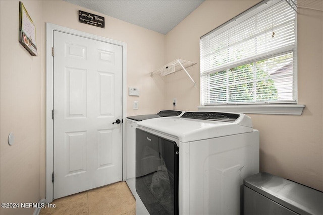 clothes washing area featuring a textured ceiling, laundry area, light tile patterned flooring, and washing machine and dryer