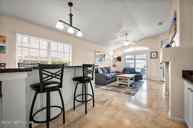 living area featuring a ceiling fan, visible vents, vaulted ceiling, and a textured ceiling