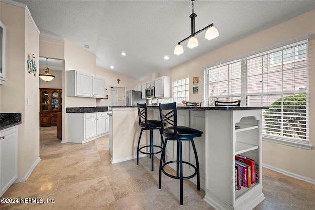 kitchen with appliances with stainless steel finishes, a textured ceiling, decorative light fixtures, white cabinets, and a breakfast bar area