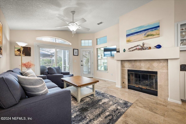 living room featuring ceiling fan, lofted ceiling, a textured ceiling, and a tile fireplace