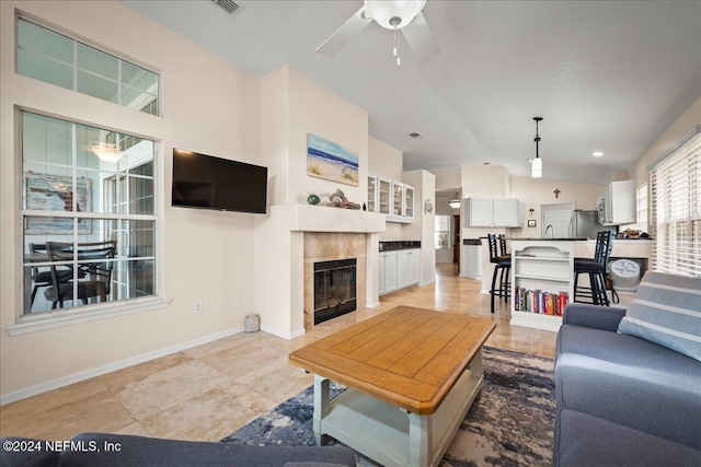 living room with a tiled fireplace, ceiling fan, light tile patterned floors, and a textured ceiling