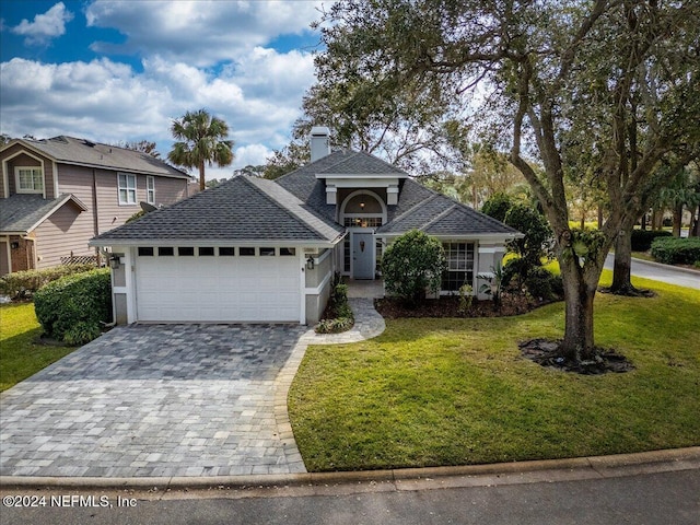 traditional-style house featuring a garage, a shingled roof, decorative driveway, a chimney, and a front yard