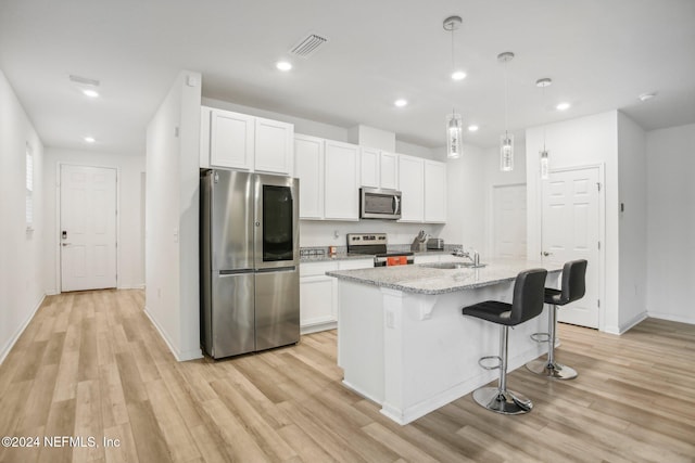 kitchen featuring white cabinets, light wood-type flooring, stainless steel appliances, and a center island with sink