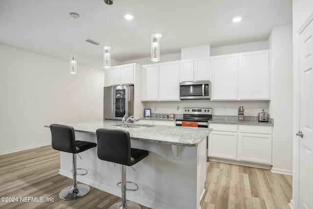 kitchen featuring hanging light fixtures, an island with sink, appliances with stainless steel finishes, light hardwood / wood-style floors, and white cabinetry