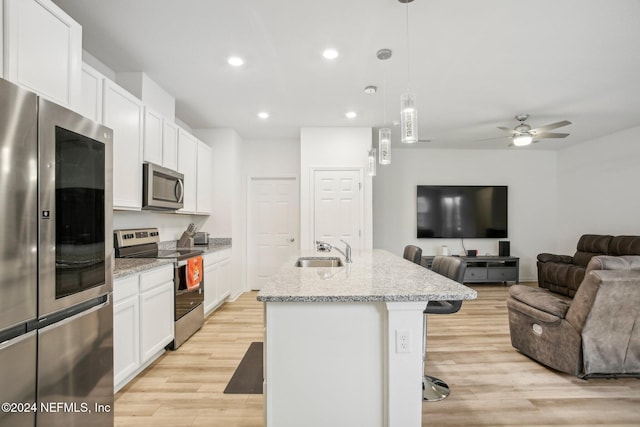 kitchen with a breakfast bar, stainless steel appliances, pendant lighting, a center island with sink, and white cabinets